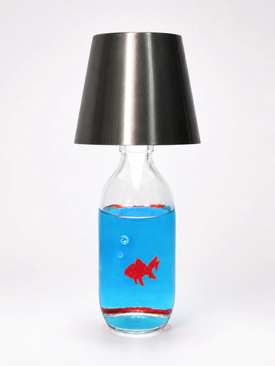 clear glass bottle table lamp with a brushed gunmetal shade and a red goldfish floating in blue liquid