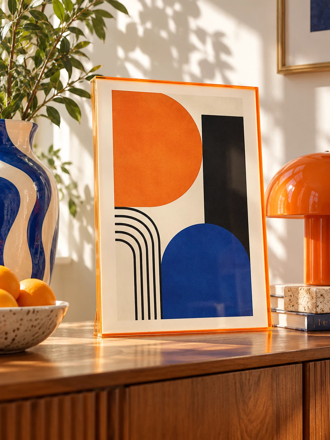 orange tinted acrylic frame with arch print beside a fruit bowl and striped vase