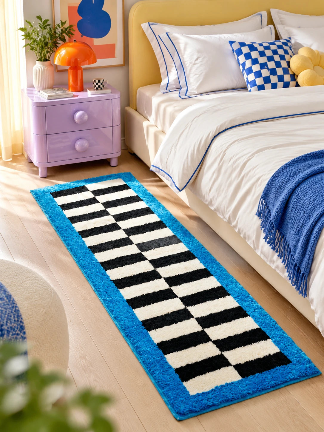Checkerboard runner rug beside a bed with a yellow headboard and a lilac nightstand on a wood floor