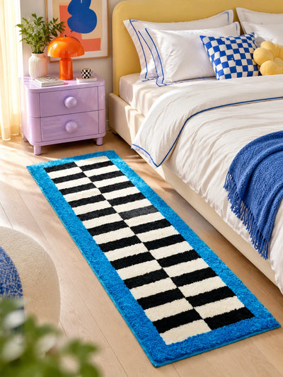 Checkerboard runner rug beside a bed with a yellow headboard and a lilac nightstand on a wood floor