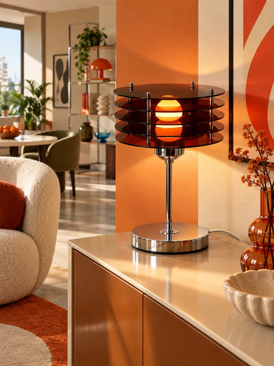 Acrylic disc table lamp glowing on a cream counter against an orange wall with an amber vase