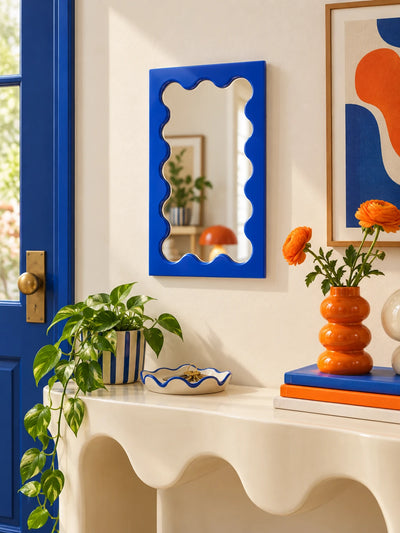Cobalt blue wavy vanity mirror above a styled console with decor objects
