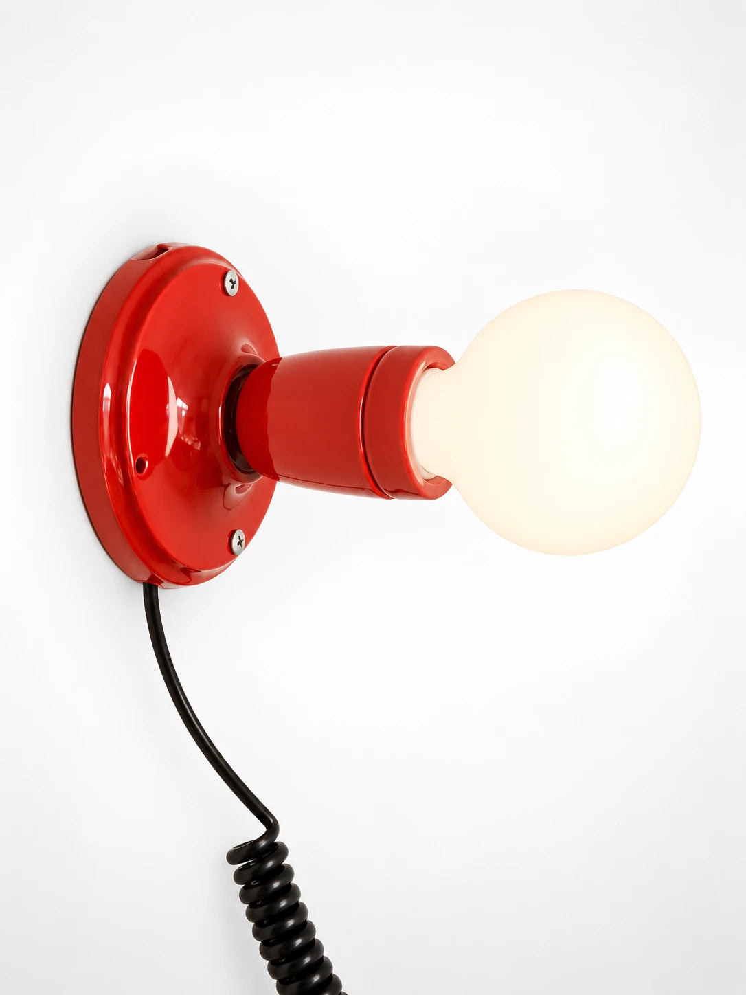 red ceramic wall light with an opal globe bulb and coiled black cord, studio shot on white
