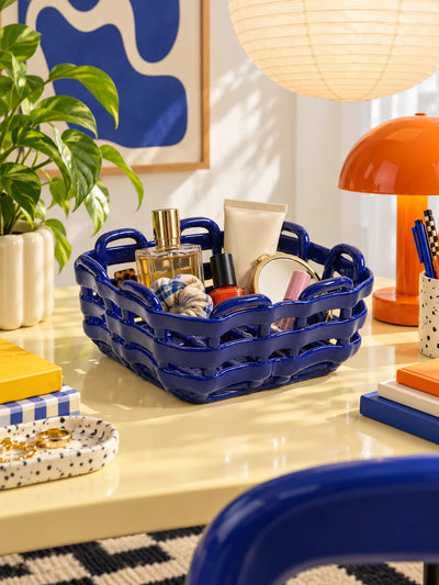 Woven ceramic basket organizing perfume and cosmetics on a desk with an orange lamp