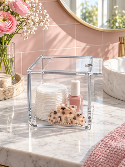clear acrylic sliding-lid box with cotton pads and nail polish on a marble bathroom counter