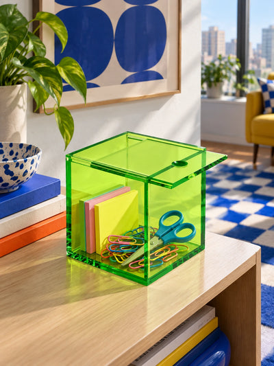 green acrylic box holding sticky notes, scissors and paper clips on a console