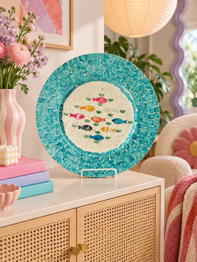 Shell mosaic fish tray on a rattan sideboard with pink flowers and pastel books