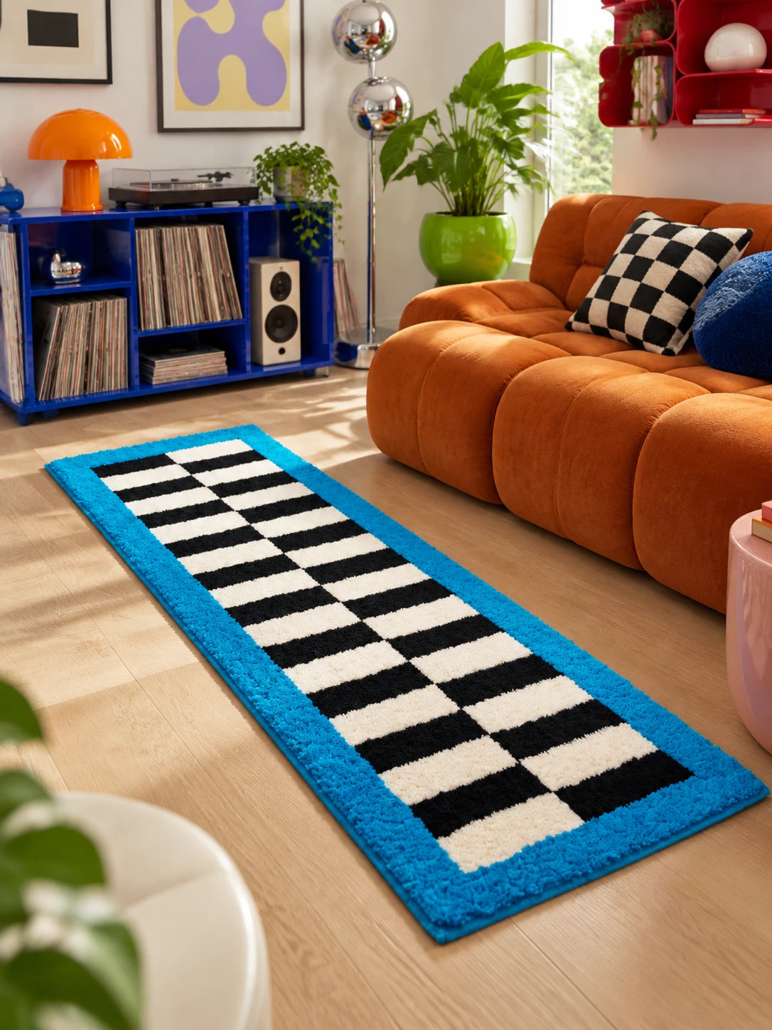 Blue border runner rug on a wood floor by a rust channel sofa, a blue record shelf and a turntable