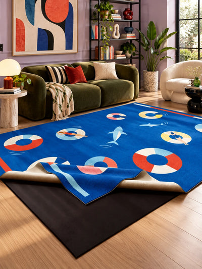 Cobalt swim ring rug in front of an olive green velvet sofa in a lilac living room with a black shelf