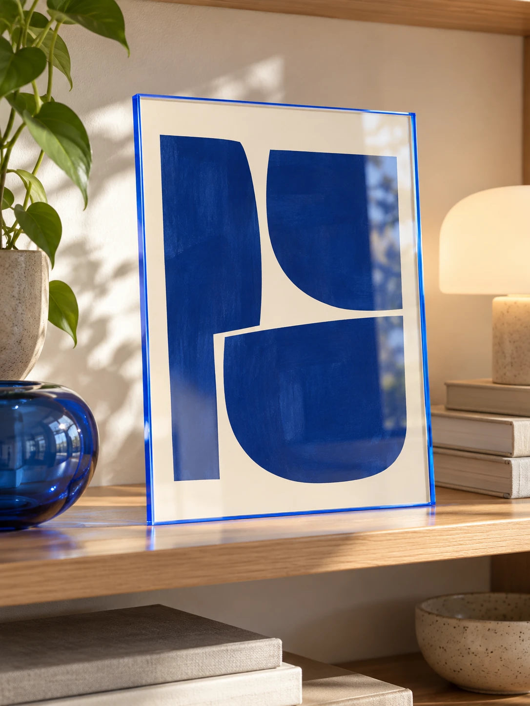 
blue tinted acrylic frame with navy abstract print leaning on a wood shelf