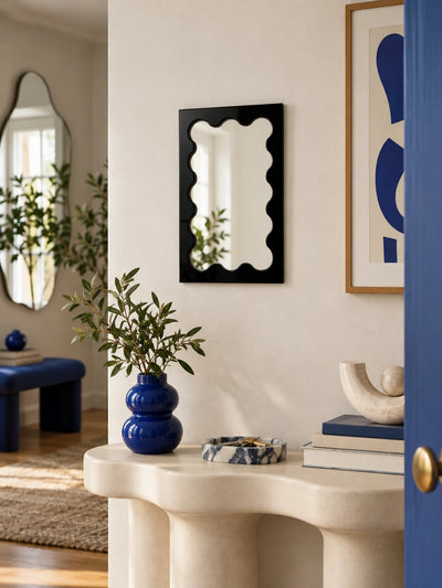 Black wavy vanity mirror against a colorful styled wall