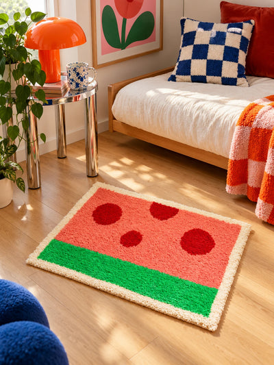 watermelon mat on wood floor in front of a cream daybed with checkered pillows