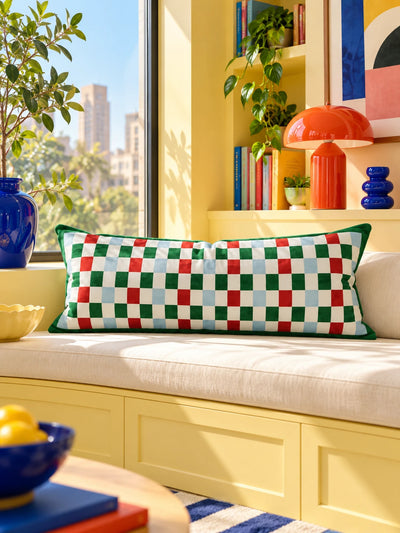Red, green and blue checkerboard lumbar pillow on a cream window seat against a yellow wall