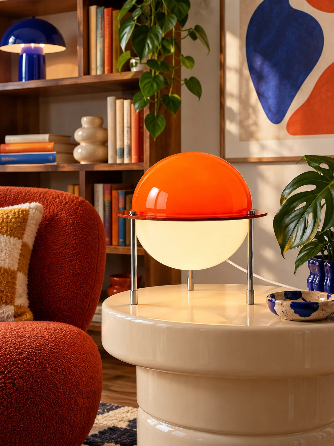 Split-sphere table lamp glowing on a cream side table beside a rust boucle armchair