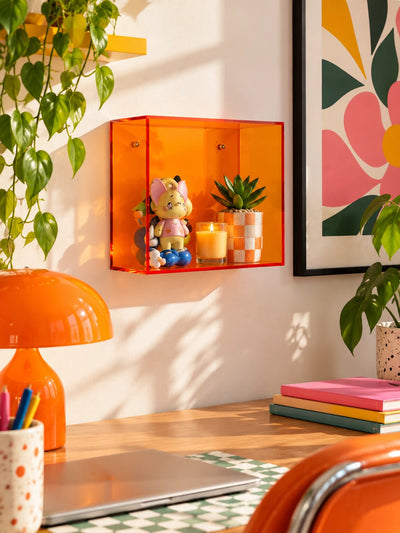 orange acrylic wall display box with figurine, candle and checkered pot above a desk