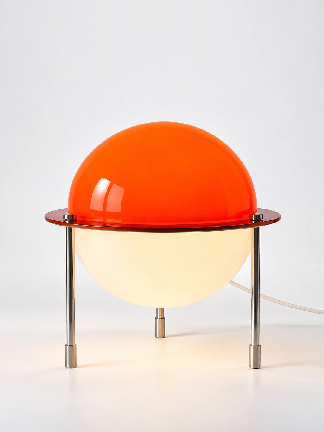 Space age table lamp with orange acrylic dome over a lit opal hemisphere on steel tripod legs