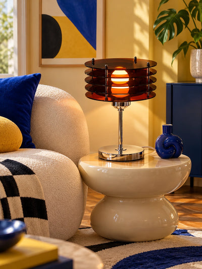 Smoked acrylic disc lamp on a cream side table beside a boucle chair and a cobalt knot vase