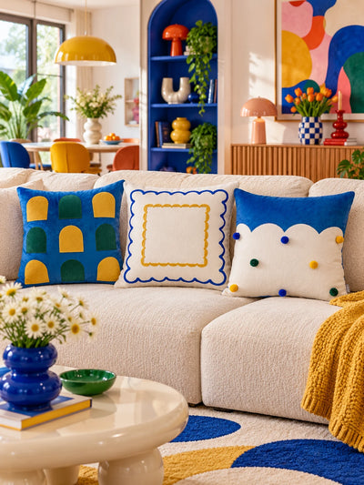 Window, scallop and cloud-edge throw pillows lined up on a cream sofa with a mustard throw and blue shelving