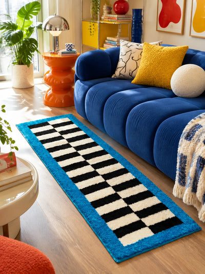 Checkerboard runner rug beside a cobalt channel sofa with an orange side table and a yellow pillow