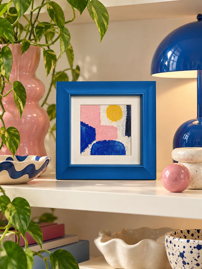 blue solid wood frame with pink and blue abstract standing on a white shelf