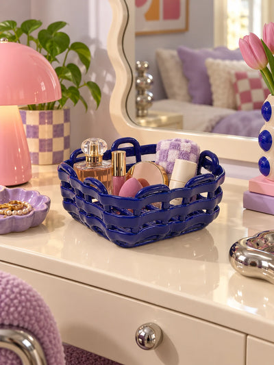 Blue woven ceramic basket of makeup on a vanity with a pink mushroom lamp