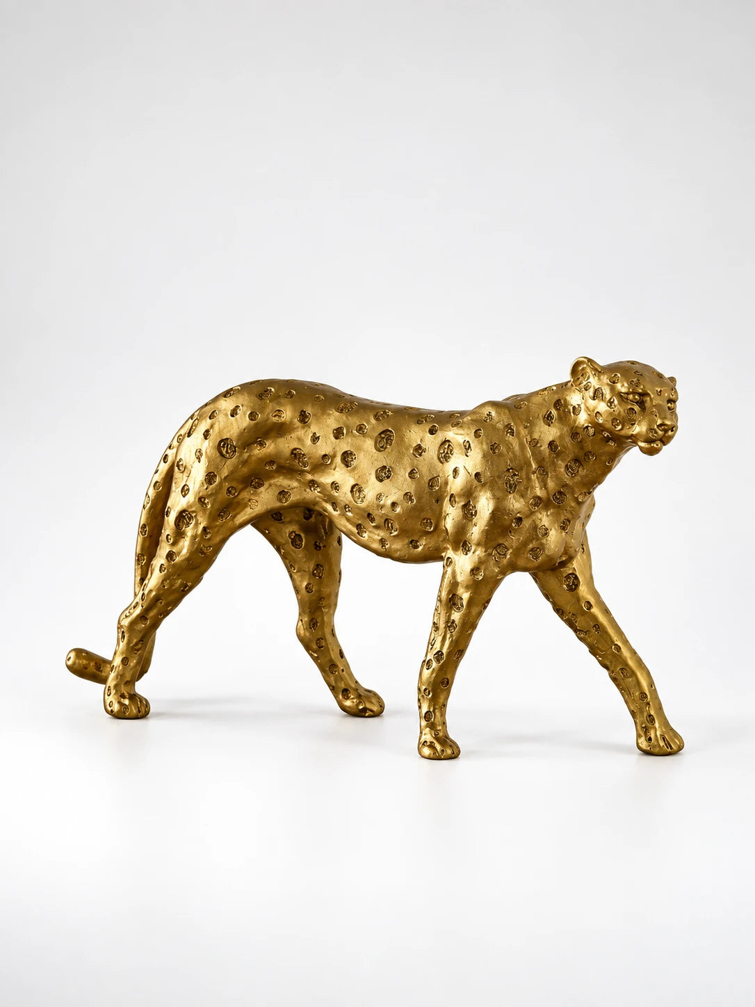 
gold-finish resin cheetah statue with hammered spots in a walking pose, studio shot on white