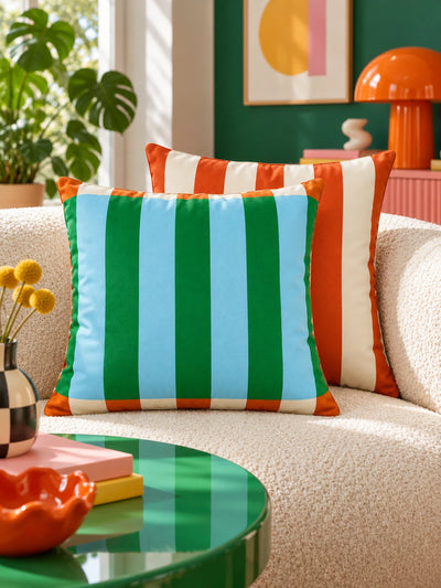 Green and blue striped pillow with orange striped pillow on a boucle sofa and green lamp behind