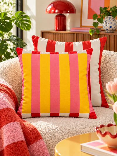 Yellow and pink striped pillow with red striped pillow by a wood slat cabinet and red lamp
