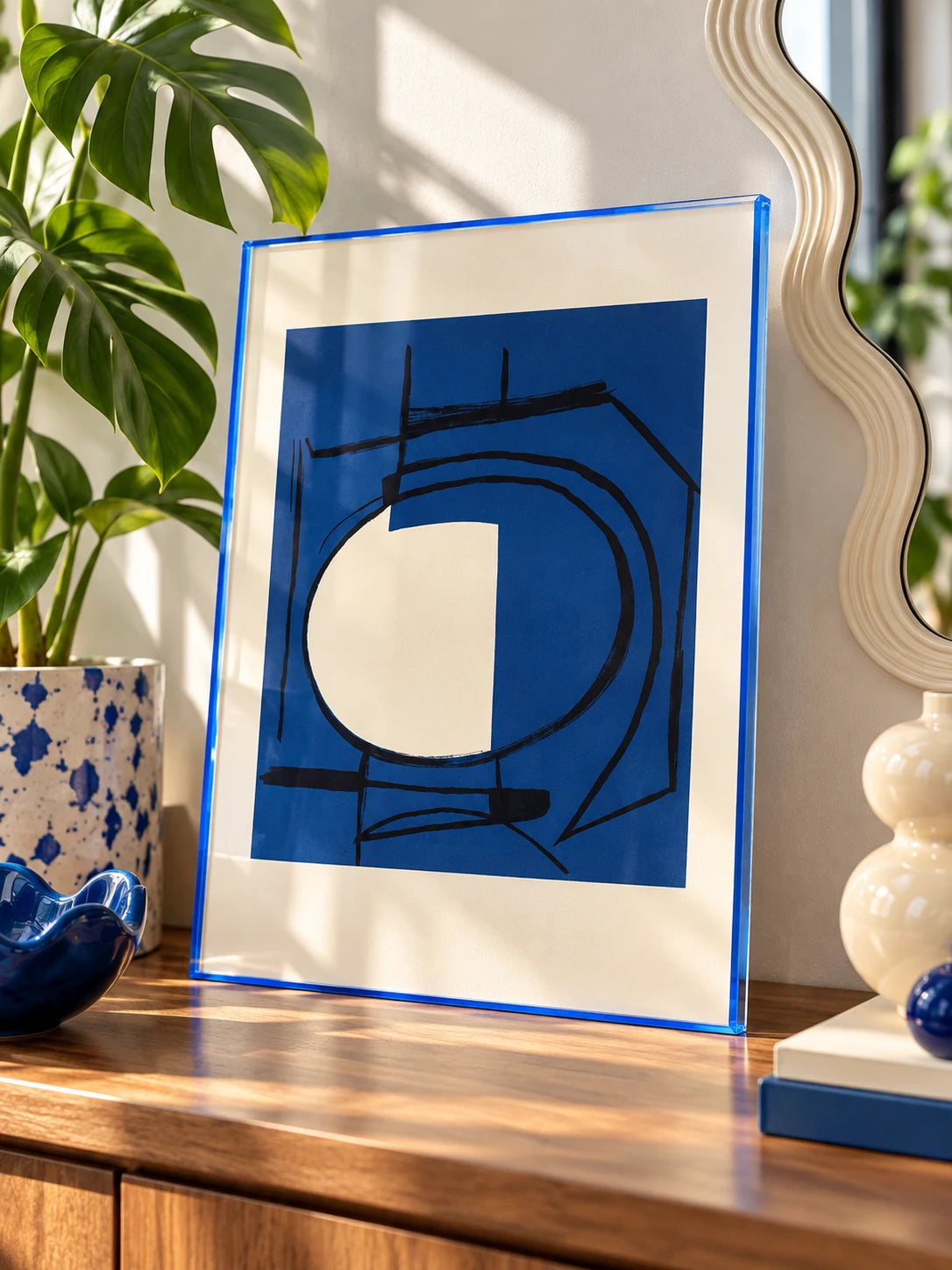 blue tinted acrylic frame with ink abstract print beside a monstera plant