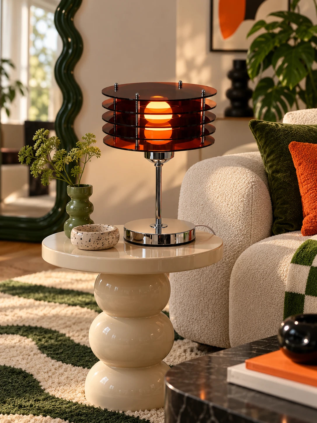 Amber acrylic disc lamp on a cream stacked side table next to a green velvet pillow and wavy rug
