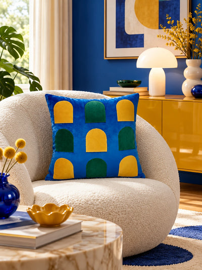 Cobalt window-arch velvet pillow on a round cream boucle chair beside a glossy yellow sideboard