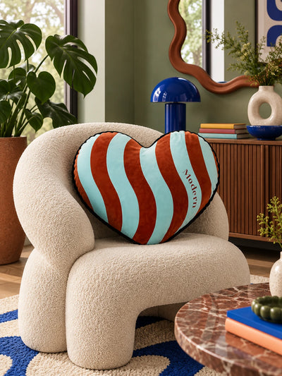 Aqua and rust heart pillow on a cream boucle armchair beside a wavy mirror