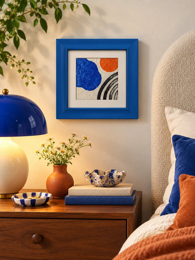 blue wood frame with abstract art on a nightstand beside a cobalt mushroom lamp