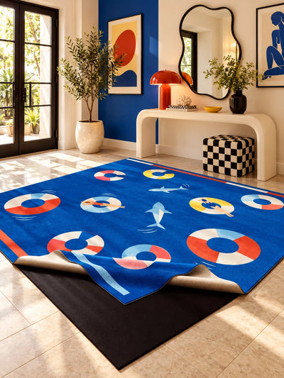 Swim ring area rug on cream stone tiles by a cobalt wall, curved console, orange lamp and checkered pouf