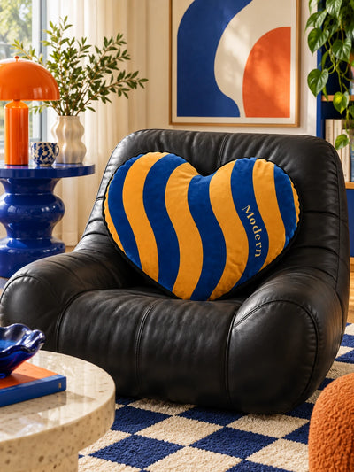 Cobalt and marigold heart pillow on a black leather chair with a blue side table