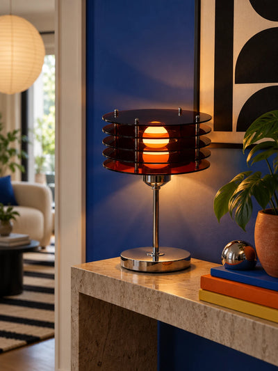 Amber acrylic disc table lamp glowing on a stone console against a cobalt wall beside a chrome sphere