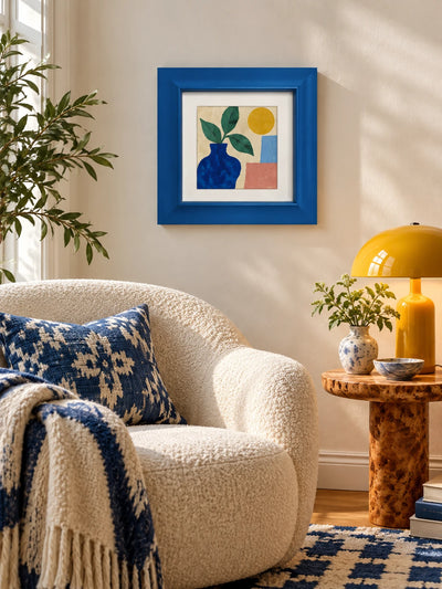 blue wood frame with vase illustration above a boucle armchair and burl side table