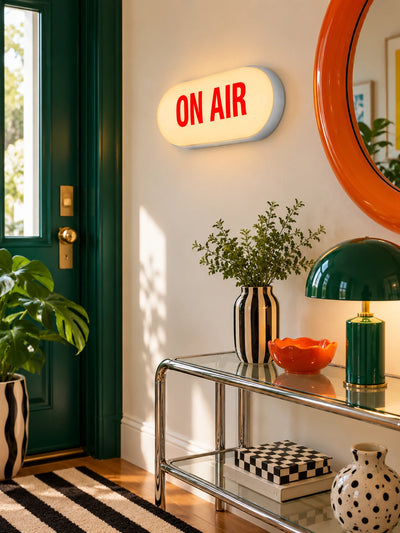ON AIR light box sign in an entryway with green door, glass console and round orange mirror
