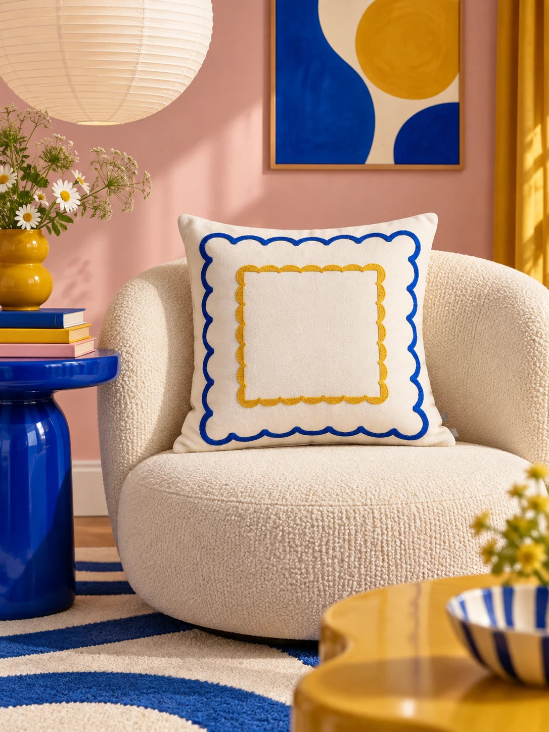 Double scallop throw pillow on a cream boucle armchair against a pink wall with a paper lantern