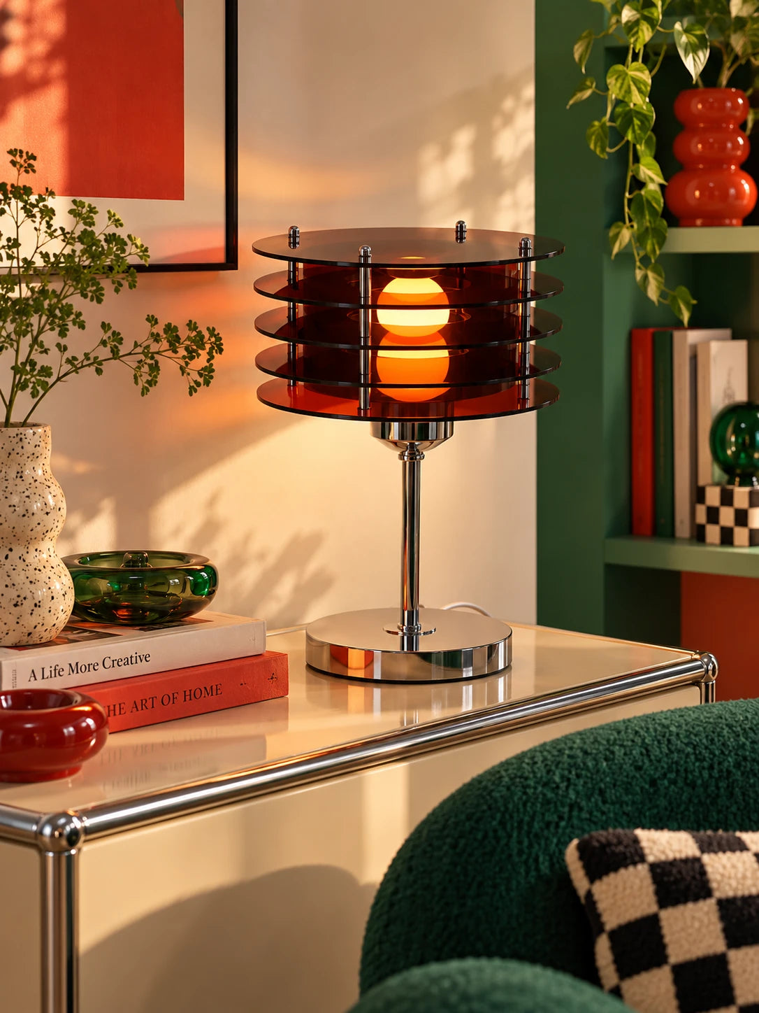 Acrylic disc table lamp on a cream cabinet with a green glass bowl, stacked books and a checkered pillow