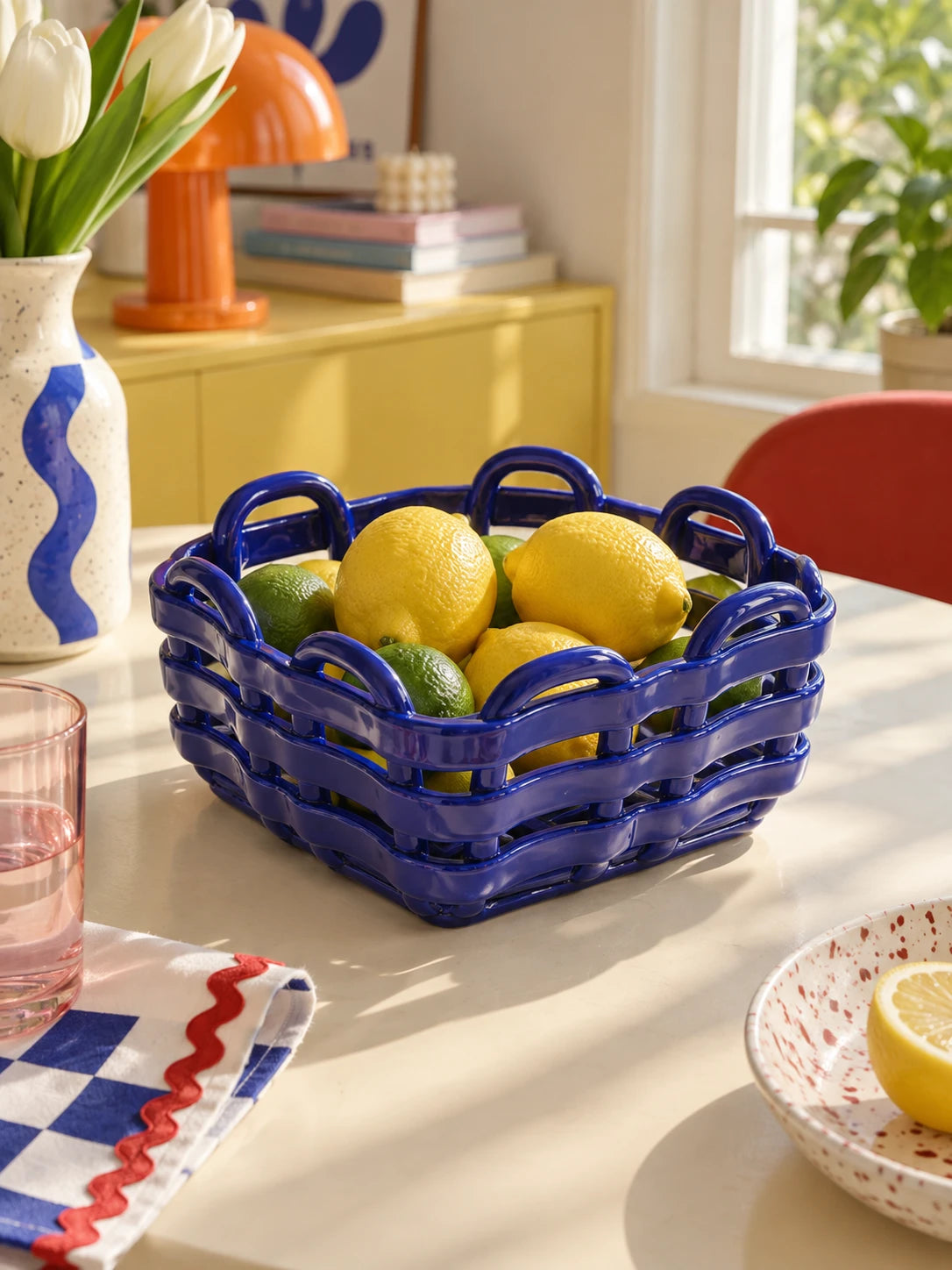 
Blue woven ceramic basket holding lemons and limes on a dining table with tulips