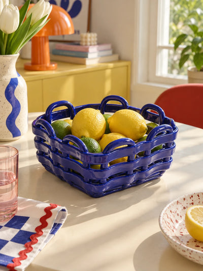 Blue woven ceramic basket holding lemons and limes on a dining table with tulips