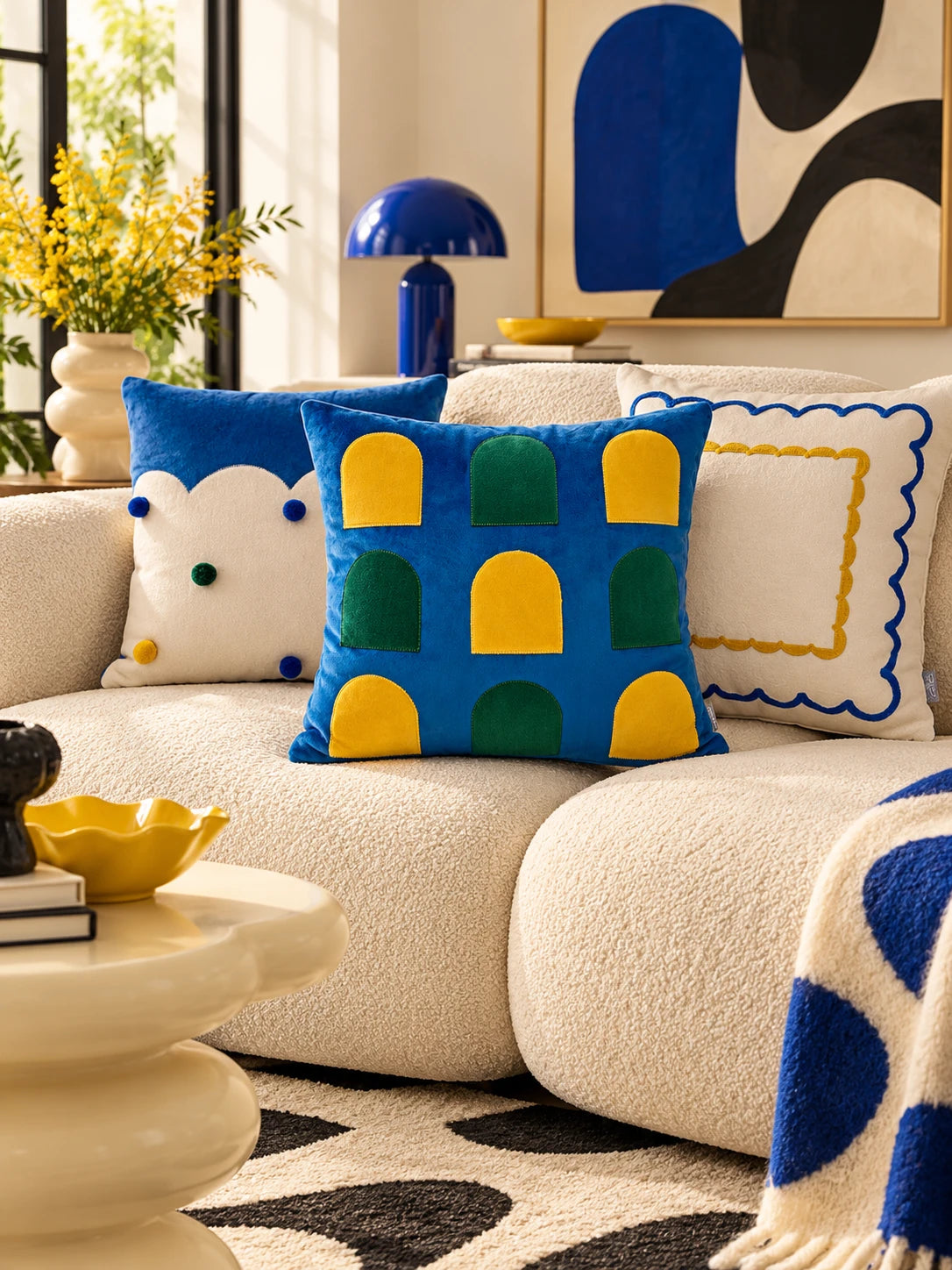 
Three cobalt and yellow throw pillows on a cream boucle sofa beside a blue mushroom lamp and abstract art