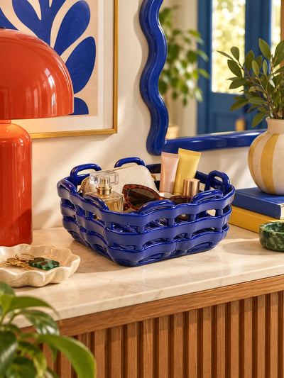 Blue ceramic basket holding perfume and sunglasses on a console with a red lamp