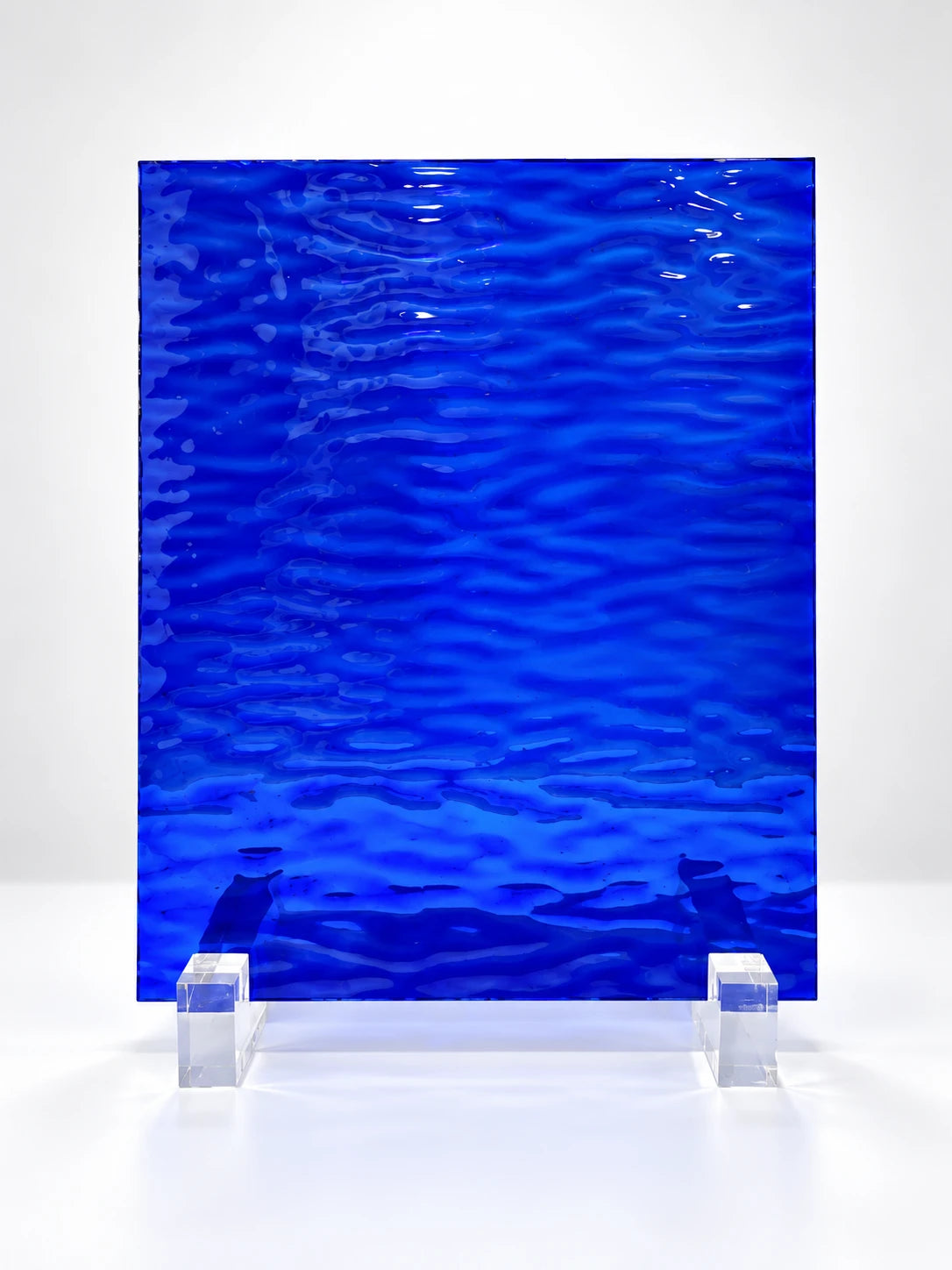 
deep cobalt blue water-ripple art glass sheet on clear stands, studio view