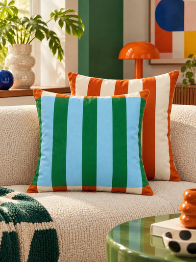 Green and blue striped pillow with orange striped pillow near an orange mushroom lamp