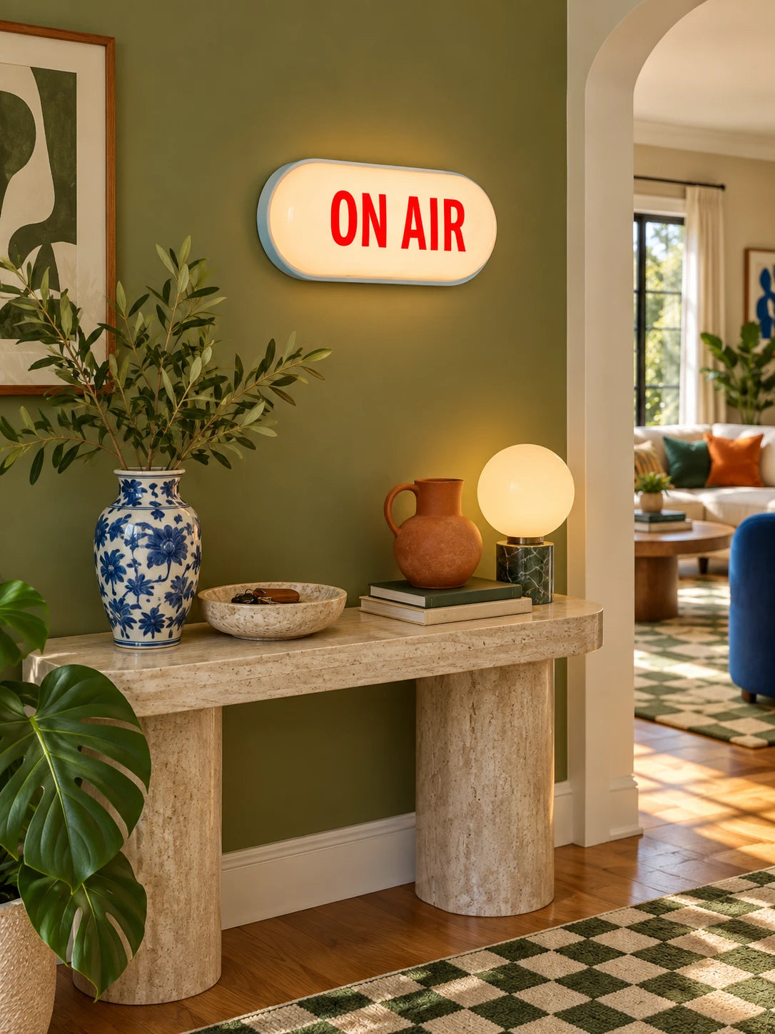 Capsule ON AIR sign on an olive wall above a travertine console with blue and white vase