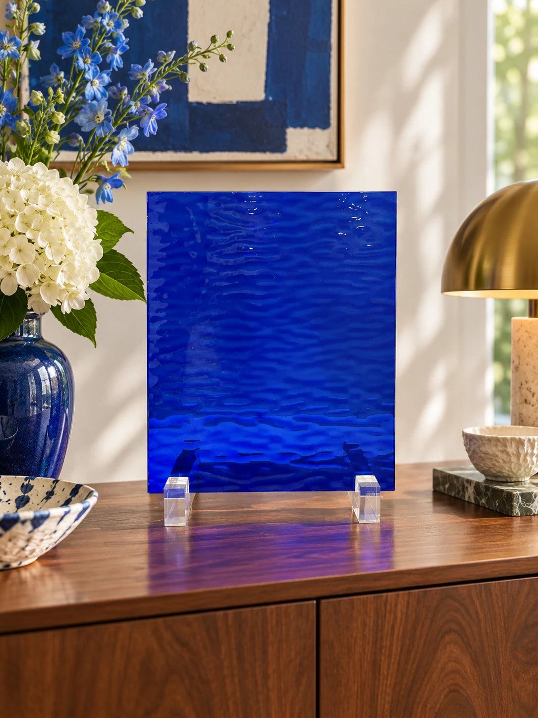cobalt rippled glass sheet on a wood sideboard with hydrangeas and a brass lamp