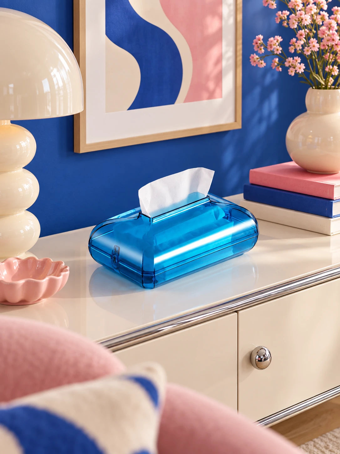 Blue jelly acrylic tissue box on a cream console against a cobalt wall with flowers