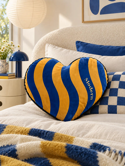 Blue and marigold heart pillow on a cream bed with a checkered blanket
